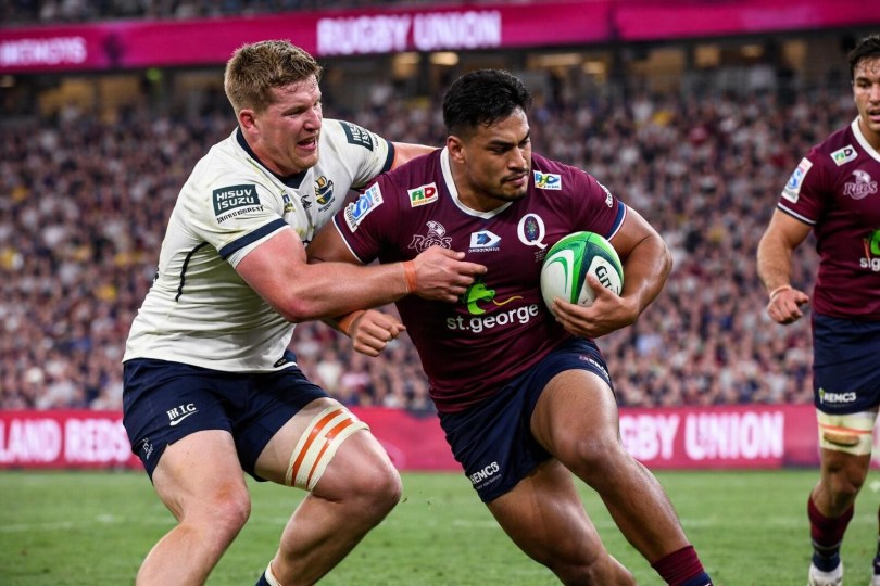 Rugby player in maroon jersey holding ball while being tackled by player in white jersey